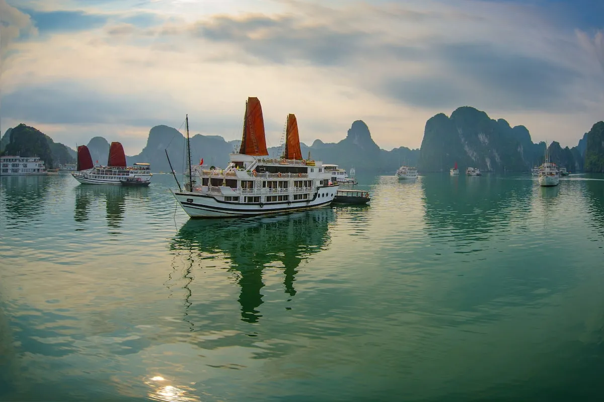 Cruise ship sailing through limestone formations in Ha Long Bay during April sunset